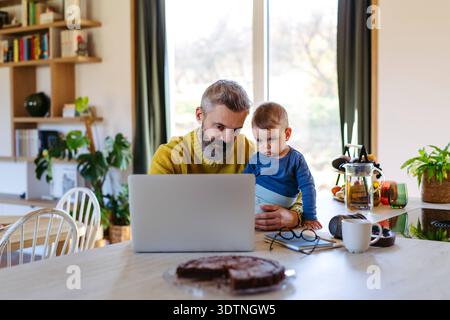 Dad working from homeoffice and taking care of toddler. Dad working from home and taking care of his toddler son. model released Stock Photo