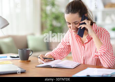 Happy freelance worker talking on phone checking agenda working at home Stock Photo
