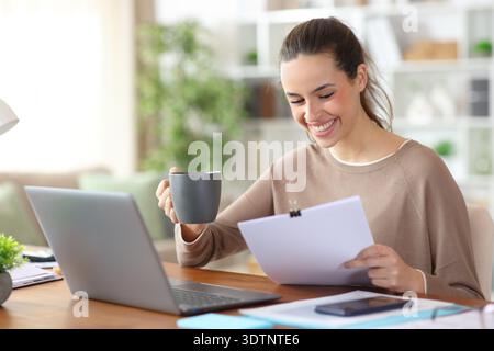 Happy self employed working online reading paper documents and drinking coffee at home Stock Photo