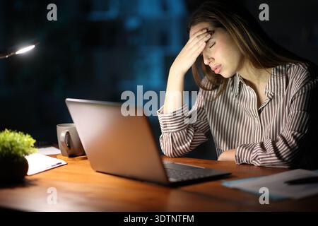 Tired freelance worker working online using laptop in the night suffering headache Stock Photo