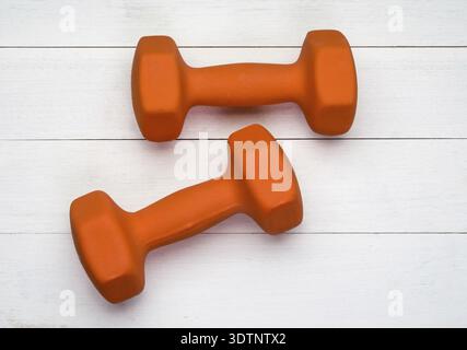 Two orange plastic coated dumbbells on white wooden background Stock Photo