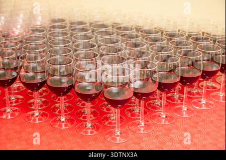 Multiple red wine glasses arranged in neat rows on a red tablecloth, ready for a reception or tasting event. Elegant hospitality concept ideal for cat Stock Photo