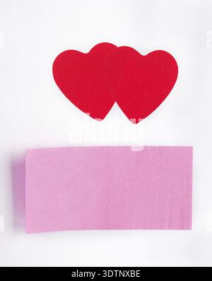 Two red hearts and a sticky-note stuck on paper sheet Stock Photo