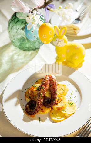 Gourmet grilled octopus with potatoes served on elegant Easter table. Festive spring seafood dish with holiday decorations Stock Photo