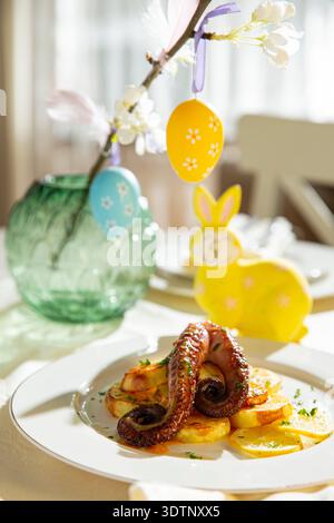 Gourmet grilled octopus with potatoes served on elegant Easter table. Festive spring seafood dish with holiday decorations Stock Photo