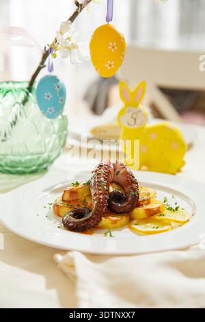 Gourmet grilled octopus with potatoes served on elegant Easter table. Festive spring seafood dish with holiday decorations Stock Photo