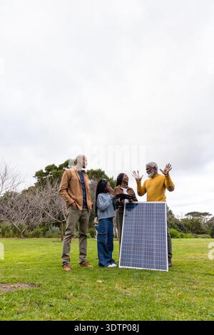 African American family examining solar panel on lawn, senior gesturing while child watching tablet Stock Photo