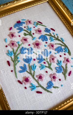 Framed floral hand embroidery on linen fabric arranged on rustic blue wooden background with threads, scissors and lace. Flat lay handmade craft compo Stock Photo