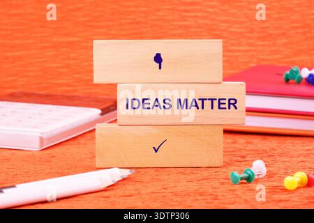 Three natural wooden blocks stand stacked on a vibrant orange desk. Stock Photo