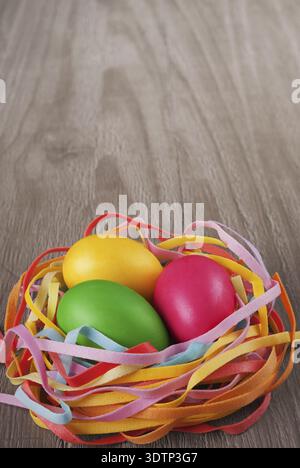 Multicolored easter eggs in the nest on old wooden table Stock Photo