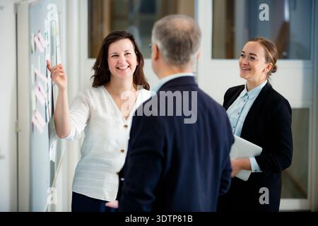 Smiling female mentor presenting project results on a whiteboard to her professional team. Positive corporate culture, successful leadership concept. Stock Photo
