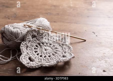 A crochet project in progress with a golden hook and light-colored yarn. Stacks of finished motifs rest on a wooden table, creating a warm and cozy ha Stock Photo