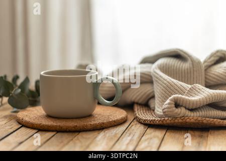 Mug on cork with knit blanket in warm home light. Cozy ritual. Stock Photo