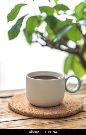 Cup of tea on cork coaster by green leaves. Cozy tea moment. Stock Photo