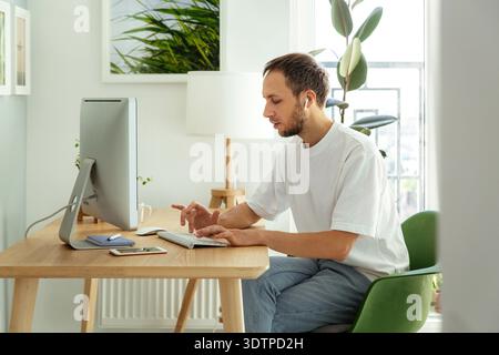 Man freelancer checking email in morning typing on wireless keyboard in home office busy with outsourcing or remote business occupation. Male freelance web developer work on computer programming app || Model released Stock Photo