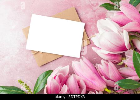 Pink magnolia flowers and green leaves with blank greeting card and envelope on pastel background. Romantic floral mockup with copy space. Mothers Day Stock Photo
