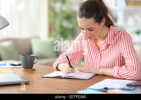 Satisfied self employed writing in paper agenda working at home Stock Photo