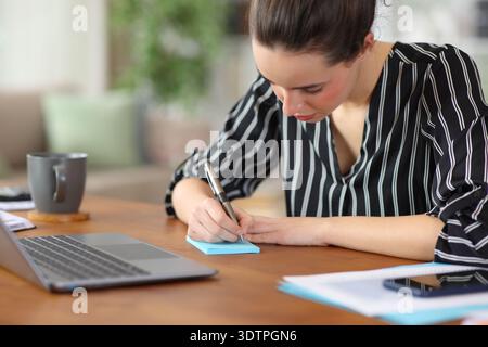 Freelance worker writing in blue sticky note in a desk working at home Stock Photo