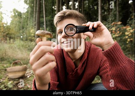Smiling man looking through magnifying glass at wild mushroom Stock Photo