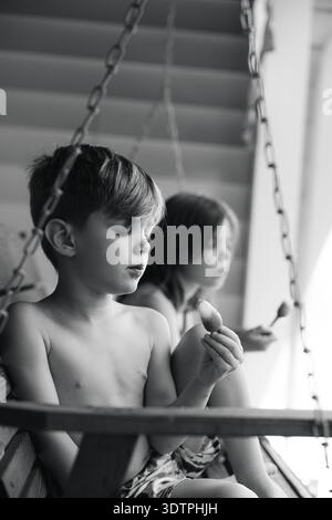 Two children sitting on porch swing eating popsicles Stock Photo