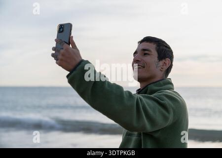 Young man taking selfie on beach using smartphone Stock Photo