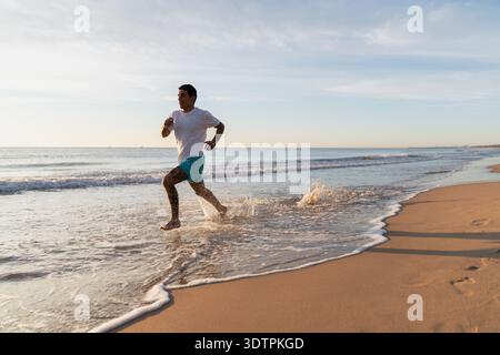Man jogging barefoot along beach splashing ocean water Stock Photo