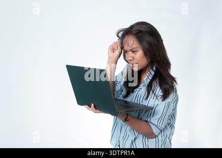 Indonesian woman with a striped shirt lifting her spectacles to look closely at her laptop. Confused or serious analytical expression. Isolated on whi Stock Photo