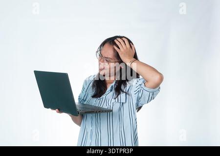 Portrait of an Indonesian woman with glasses and a striped shirt looking at her laptop with a stressed expression, holding her head in frustration. Is Stock Photo