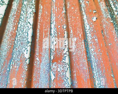 A low-angle perspective of a weathered orange corrugated metal wall. Features leading lines of vertical ridges with flaking blue and white paint, rust Stock Photo