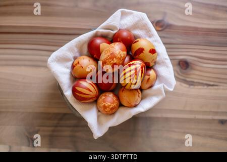 Easter tradition, naturally dyed eggs, leaves, home decoration, craftsmanship, creative activity, white basket, rustic, wooden table. Stock Photo