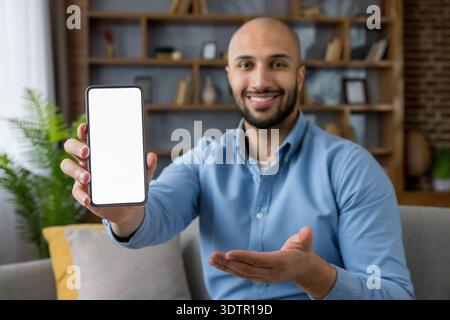 Male professional holds modern smartphone with blank white screen for app or website mockup, ideal for digital marketing, tech promotion, user interface or mobile content in a home setting Stock Photo