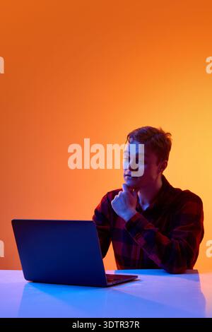 Young professional analyzing data on laptop against gradient background. Stock Photo