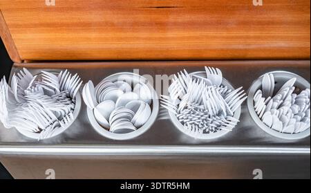 Fast-food disposable tableware. Plastic cutlery. Many white disposable plastic spoons, forks and knifes in holder at cafeteria Stock Photo