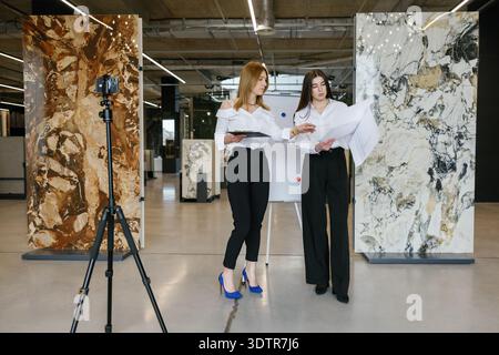 Professional female architects collaborating on interior design project, planning using blueprints in a modern marble and tile showroom Stock Photo