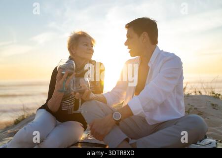 Mature couple enjoying wine at sunset on beach Stock Photo