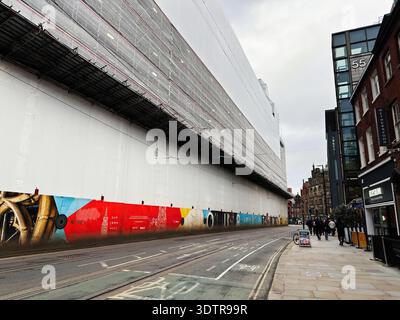 Manchester, UK - January 29, 2026: Urban street scene in Manchester shows a long white building under scaffolding beside a bright mural. Stock Photo
