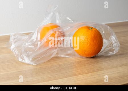 Two oranges wrapped in plastic on a wooden table, showcasing a simple, everyday scene. Stock Photo