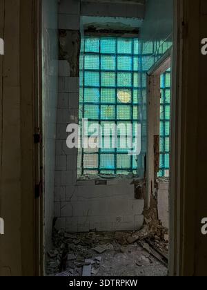 An Abandoned Passageway with Cracked Walls and a Blue Glass Block Window Casting Light on the Ruined Interior Stock Photo
