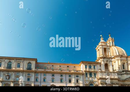 View of Sant Agnese in Agone baroque church with grand dome in Piazza Navona against blue sky with floating soap bubbles, Rome city, Italy. Travel and Stock Photo