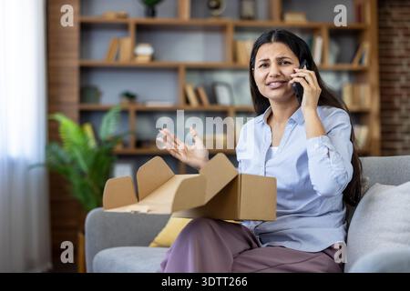 Upset woman having a phone conversation regarding a disappointing online shopping experience, holding an empty cardboard box after receiving a bad delivery Stock Photo