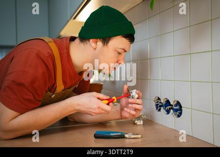 Electrician in workwear installing electrical outlets on a tiled kitchen apron, carefully connecting wires to a new power socket for improved home functionality and safety Stock Photo