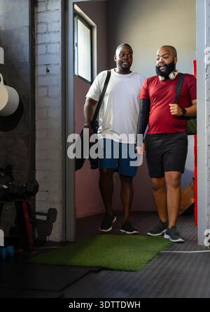 African American men walking through narrow gym doorway in sportswear carrying duffel, headphones Stock Photo