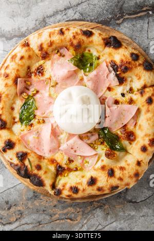 Charred pizza with mortadella sausage and burrata cheese close-up on a wooden board on a table. Vertical top view from above Stock Photo
