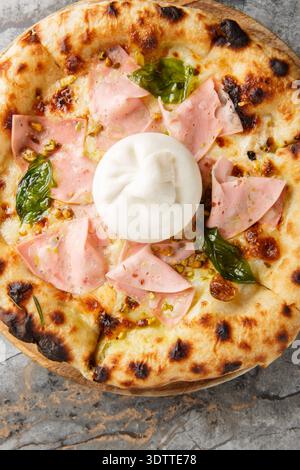Close-up of neapolitan pizza with whole burrata cheese, mortadella and crushed pistachios on wooden board. Vertical top view from above Stock Photo