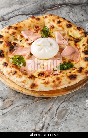 Close-up of neapolitan pizza with whole burrata cheese, mortadella and crushed pistachios on wooden board. Vertical Stock Photo