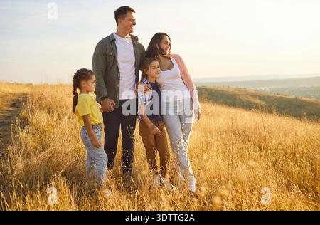 Happy family of four in golden meadow at sunset, enjoying nature together Stock Photo
