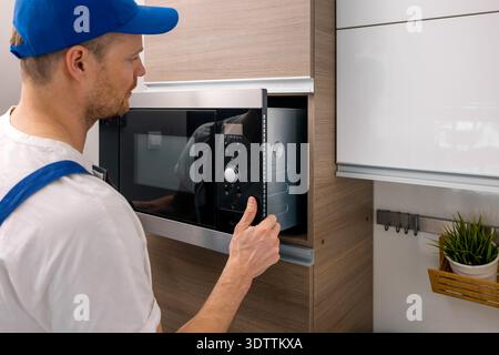 service worker installing integrated microwave oven in the domestic kitchen. household appliance maintenance and repair Stock Photo