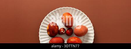 Vibrant Easter eggs in various shades of red and orange are beautifully arranged on a white plate, adding charm to the festive atmosphere of the seaso Stock Photo