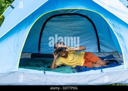 Blue dome tent is framing binoculars, green sleeping bag and dark blue mat on grass Stock Photo