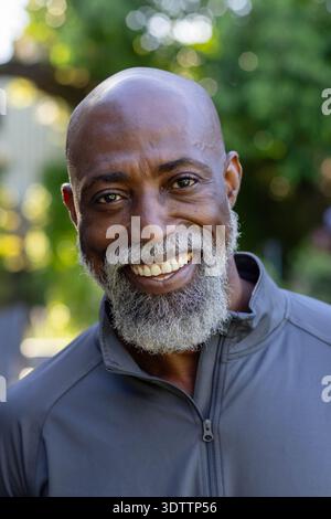 Mature African man smiling and facing camera in backyard garden wearing gray zip-up jacket, bokeh Stock Photo